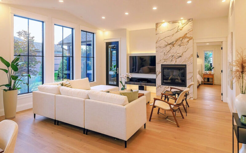 Modern living room with neutral colours and marble fireplace with an outdoor view and hallway to a beroom