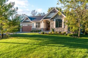 The Golden Locust Stone and siding ranch home with a wooden garage door and gabled roof, surrounded by a green lawn and trees.