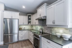The Golden Locust Modern kitchen with white cabinetry, dark countertops, stainless steel appliances, and a stone tiled backsplash.