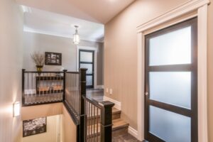 The Golden Locust Interior hallway with wood floors, black-railed staircase, and dark wood doors with frosted glass panels.