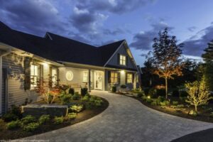 Heron Gate | Photography: © Daniel Vaughan (vaughangroup.ca) Exterior of a home at night with glowing windows, professional landscaping with lights, and a curved stone pathway.