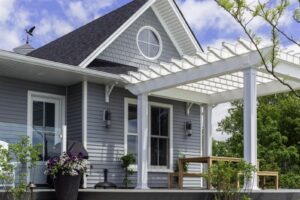 Heron Gate | Photography: © Daniel Vaughan (vaughangroup.ca) A grey shingle house with a white pergola over a wooden deck, accented by large stone steps.