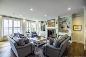 Heron Gate | Photography: © Daniel Vaughan (vaughangroup.ca) Lakeside living room with blue patterned armchairs, a white fireplace, and large windows overlooking the water.