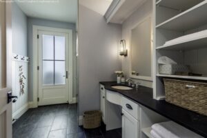 Heron Gate | Photography: © Daniel Vaughan (vaughangroup.ca) A sleek mudroom or bathroom with black countertops, white cabinets, dark slate floors, and a frosted glass door.