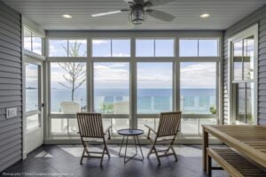 Heron Gate | Photography: © Daniel Vaughan (vaughangroup.ca) A screened-in porch with grey siding, dark tile floors, and wooden chairs looking out over a calm, blue lake.