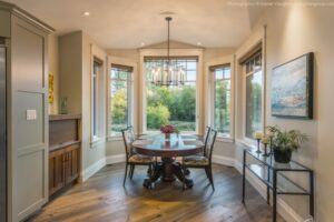 Formal dining room with a dark wood table, floral chairs, and a large bay window overlooking green trees.
