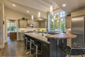 The Twisted Willow | Photography: © Daniel Vaughan (vaughangroup.ca) Contemporary kitchen with a large dark island, light grey cabinets, vaulted ceilings, and glass pendant lights.
