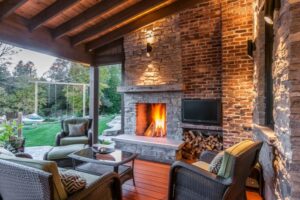 The Twisted Willow Covered outdoor patio with a roaring stone fireplace, brick accents, wicker furniture, and a view of the yard.