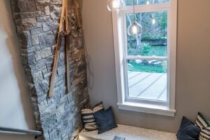 The Twisted Willow Stairwell landing featuring a built-in window seat, hanging globe lights, and vintage skis mounted on a stone wall.