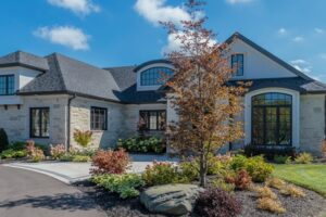 Luxury stone ranch-style home with dark gabled roofs, black-framed windows, and professional garden landscaping.