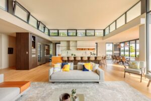 Gemini said Bright, open-concept living area and kitchen with clerestory windows, light wood floors, and a grey sofa with colorful pillows.