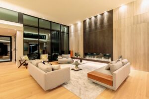 Modern living room at night with a large fireplace wall, a glass coffee table, and squared sofas