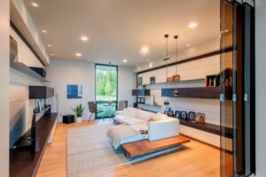 Modern living room with wood floors, white sofa, rug, and built-in shelving units, under warm ceiling lights.
