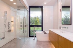 Modern bathroom with a glass shower, soaking tub by a window, and a wood floating vanity with white tiled walls.