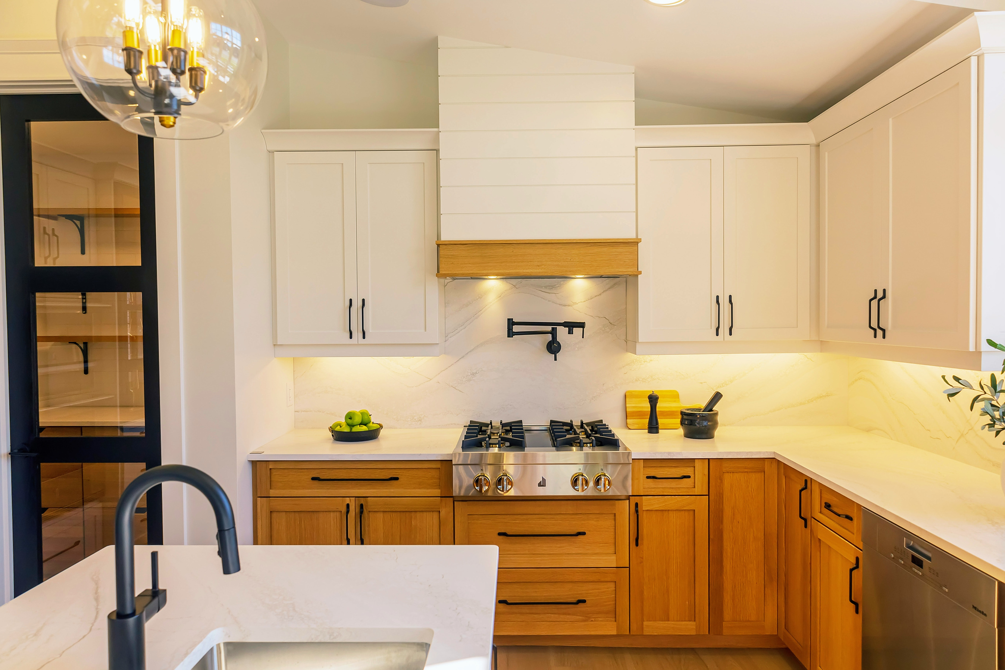 A modern kitchen featuring white upper and wood lower cabinetry, a gas range and a marble-patterned backsplash.