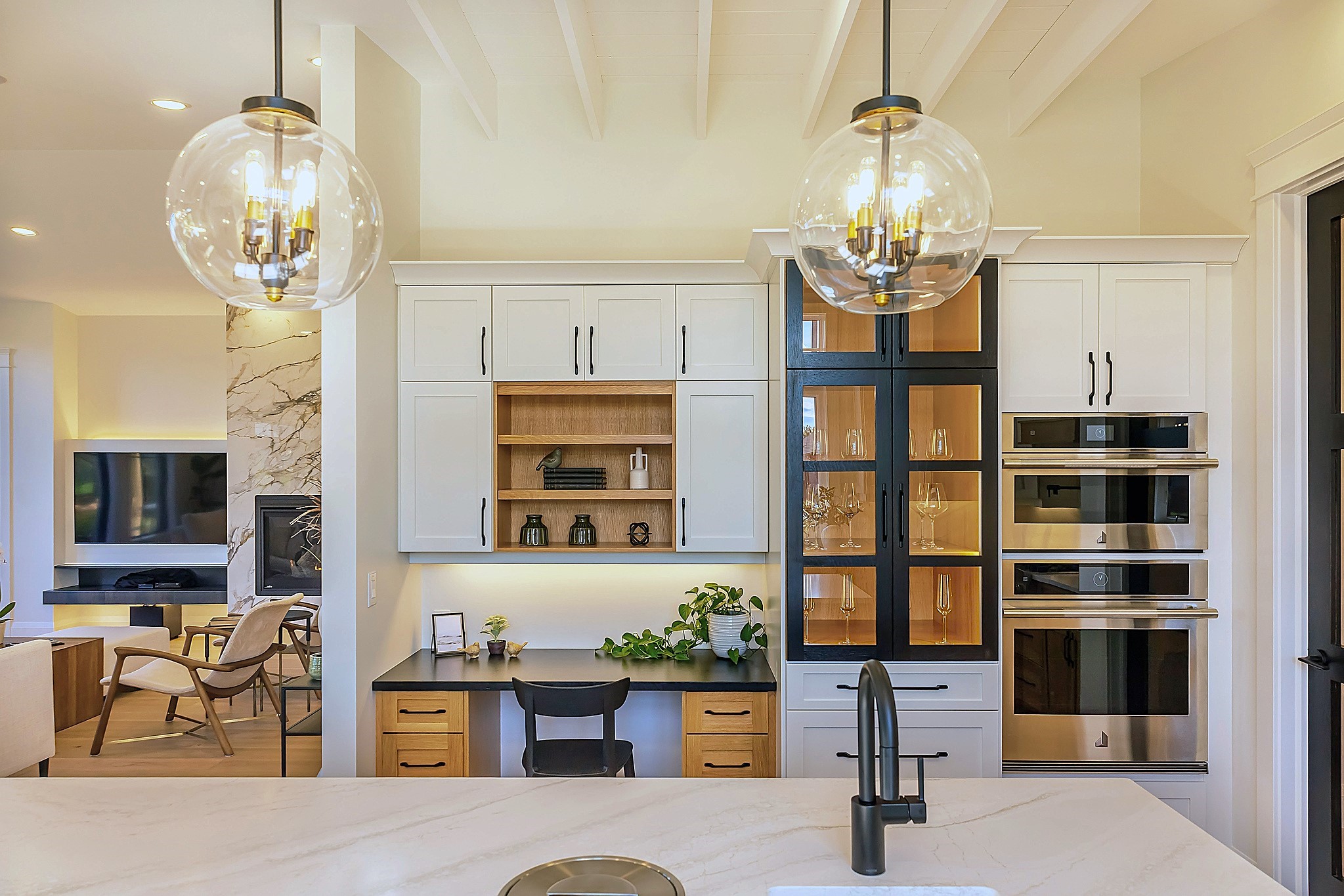 An elegant workspace within a kitchen area, including white shaker-style cabinets, a black granite desk, and a built-in display hutch with integrated lighting.