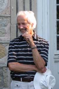 A man wearing polo t-shirt with one hand resting on chin while the other is resting across body while holding a white boonie hat
