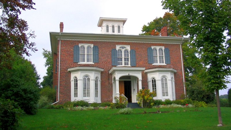 Historical two-story brick building that has covered front landing and two bay windows on each side