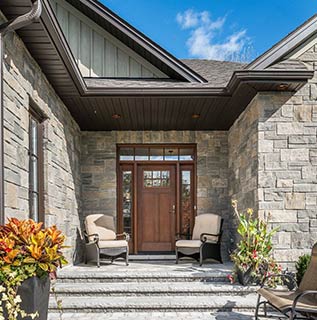 Front entrance of a stone home building with steps and two chairs outside the front door