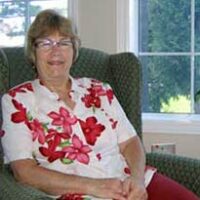 Woman wearing a white shirt with pink florals sitting in a chair smiling for photo