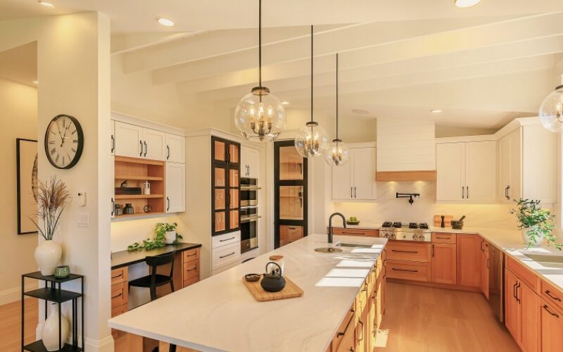 A two toned kitchen with white upper cabinets and light wood lower cabinets accented with white marble counter tops and hanging globe lights