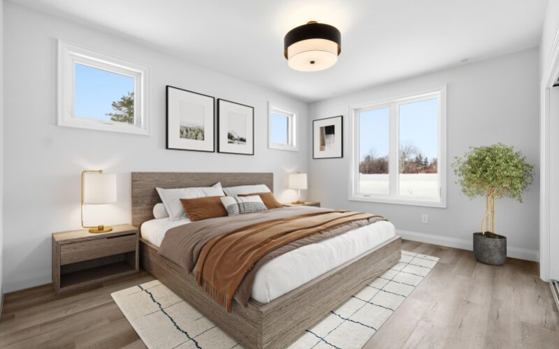 A bright, modern bedroom featuring a wood-framed bed with earth-toned bedding, two matching wooden nightstands with gold lamps, and neutral grey walls decorated with framed art.
