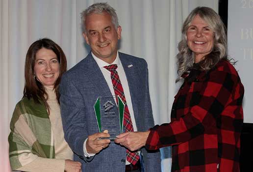 Man and woxman accepting an award made of glass as they smile for a picture with the presenter.