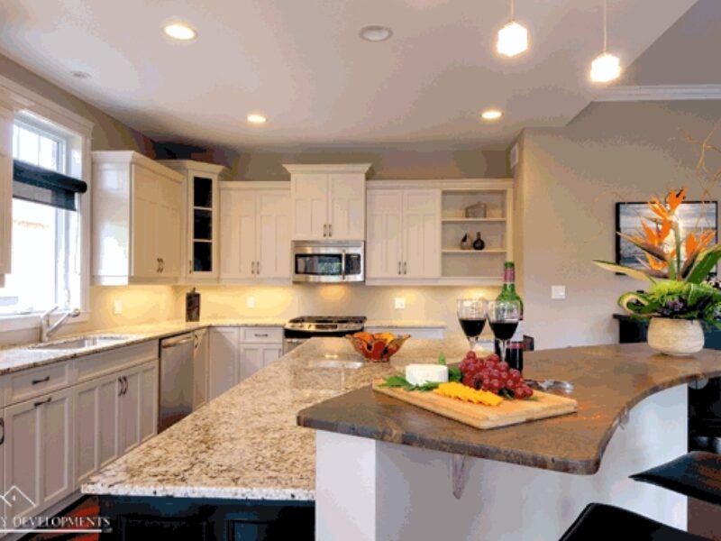 Kitchen with white cabinets and granite counter tops. A curved bar-style seating area with two stools are on the side.