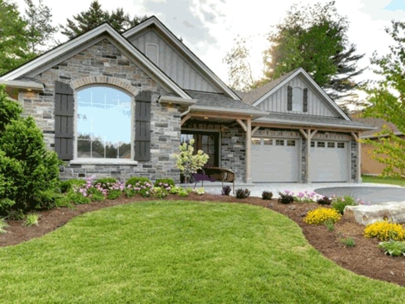 Stone house with arched window and two attached garages complimented with landscaped front grass and curved garden