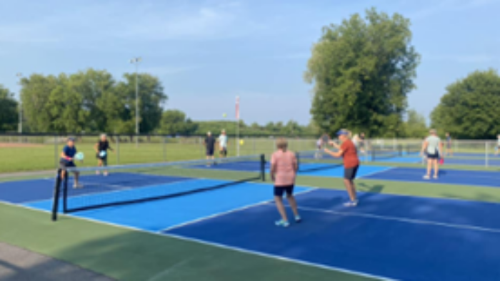 Outdoor pickleball courts with people playing on blue courts
